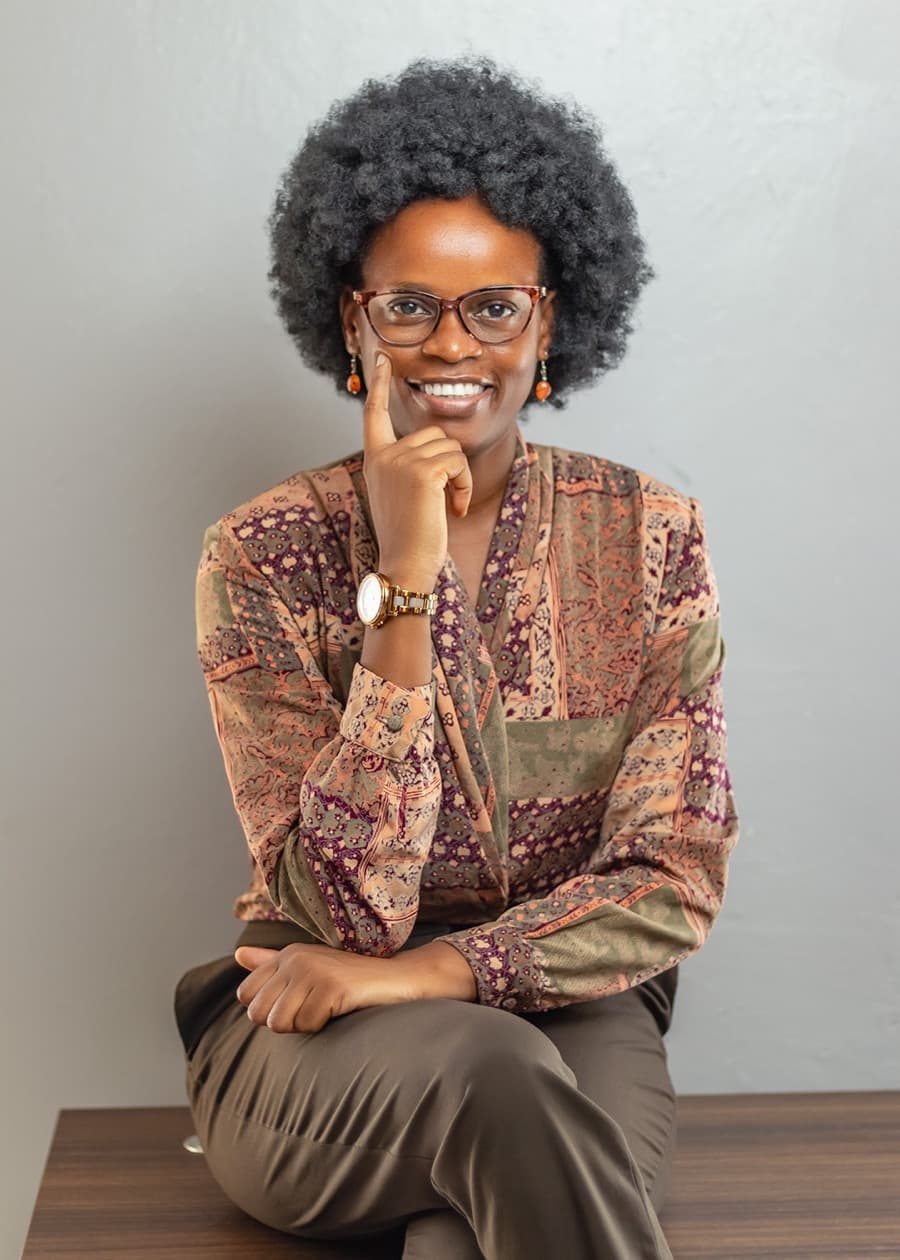 Studio portrait of Ilse Kithembe, seated and smiling, in a patterned blouse