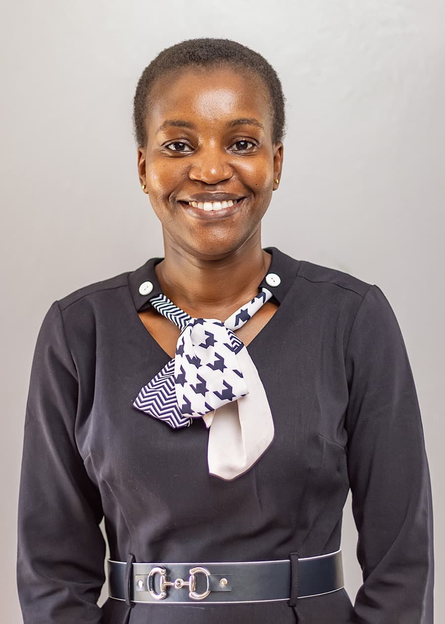 Studio portrait of Priscah Mongera, smiling, in a navy dress with a patterned neck scarf